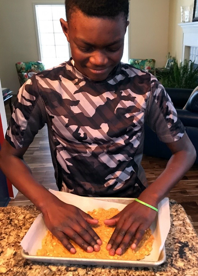 A young man patting food into a pan.