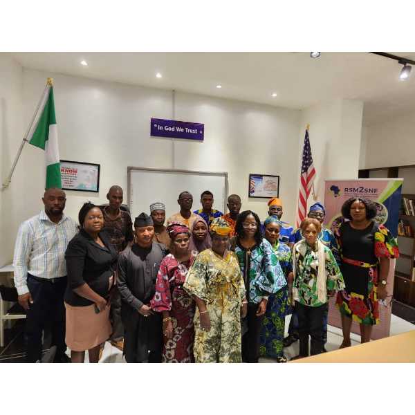 Attendees at a RSM2SNF event, three rows of people standing together in front of the Nigerian and American flags.