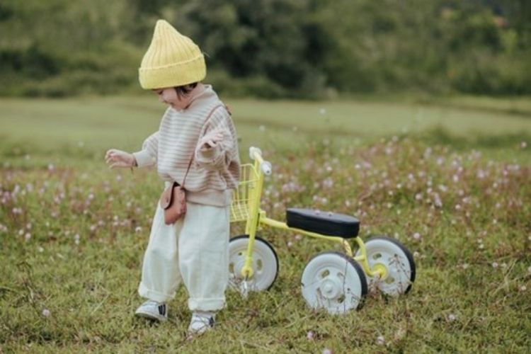 a young girl in a yellow hat standing next to a yellow bike.