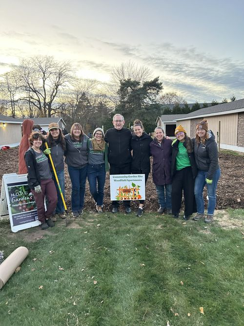 A group of people in front of a community garden sign with fallow ground behind them.