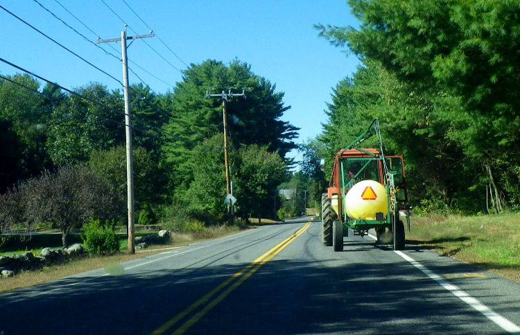 A tractor with a triangle hazard sign on the back drives down a road.