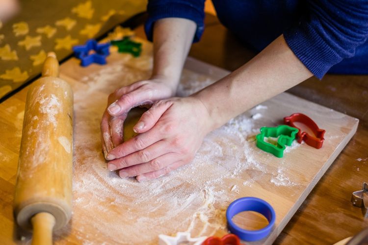 A child's hands playing with dough on a mat. On the edges of the mat are a rolling pin and cookie cutters.