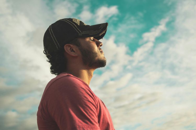 A man closing his eyes and breathing deeply outdoors.