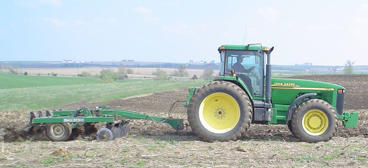 Green John Deere tractor pulling a disk harrow through a partially tilled field.