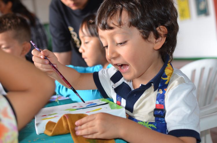 Un niño pequeño mojando un pincel en pintura.