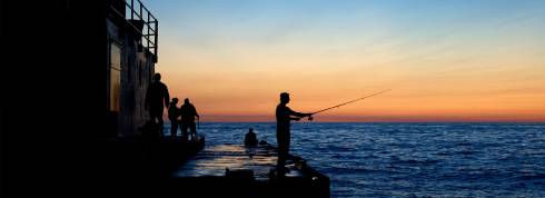 Person fishing off pier in Lake Michigan. Water is blue and the sky is a gradient of orange to blue.