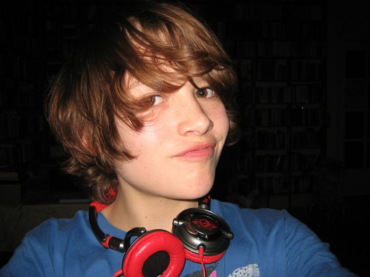 An young person with a blue shirt and headphones around his neck.