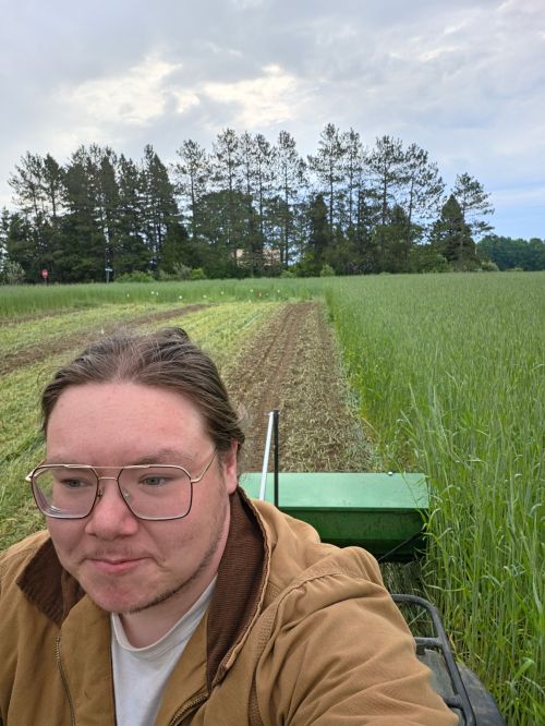 A young student drives an ATV pulling a seeder in a field.