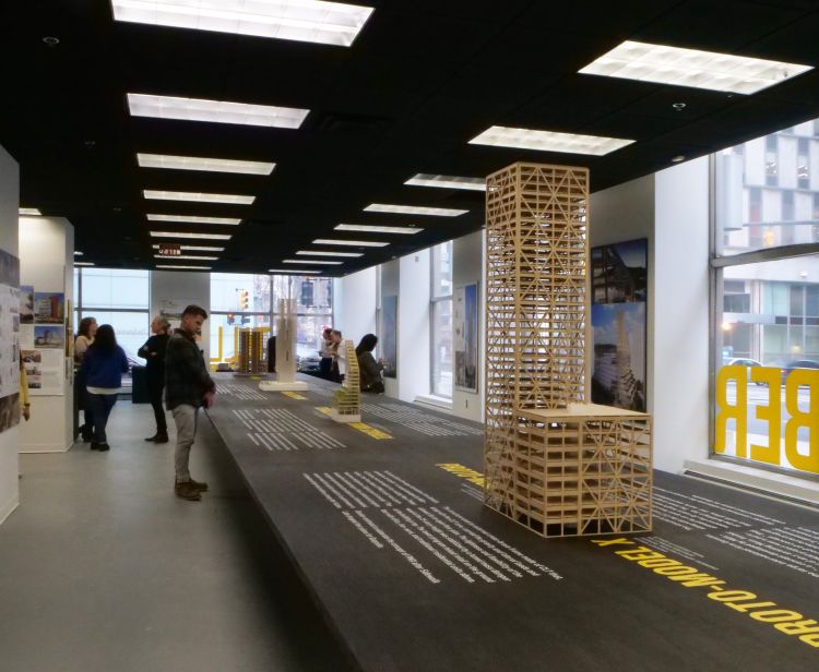 Exhibit guests standing at a long wooden table with wooden mockups of mass timber buildings.