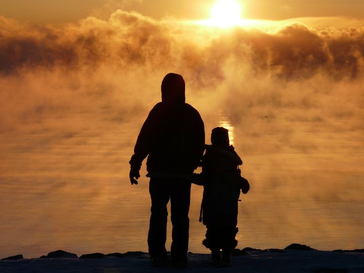 An outline of a tall person and smaller person (presumably a child) walking towards the sun on the horizon.