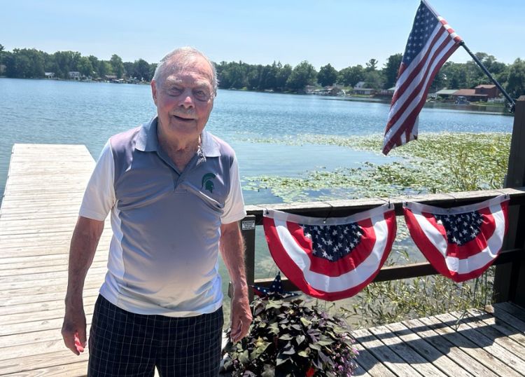 A man standing on a dock next to two red white and blue buntings and an American flag.