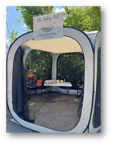 A portable tent labeled "The Baby Nest" with chairs and a table inside, set outdoors.